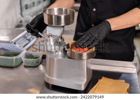 A cook using a press to make hamburger patties Royalty-Free Stock Photo #2422079149