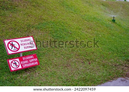 Prohibition sign for "Dilarang menginjak rumput" or "No stepping on grass" in a park