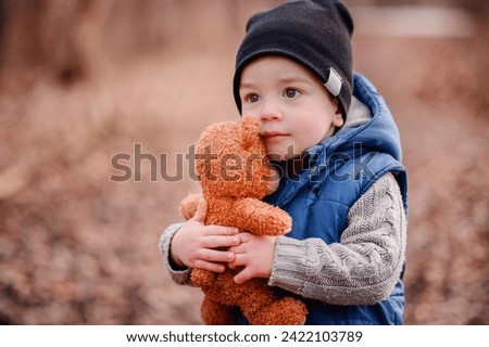 Innocent toddler clutching a teddy bear, a comforting presence on his outdoor adventure Royalty-Free Stock Photo #2422103789