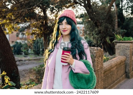 Stylish young smiling hipster woman with color hair walking on street in pink outfit with reusable coffee cup wearing coat, knitted hat, fur bag, happy mood, seasonal fashion, Barbiecore style trend Royalty-Free Stock Photo #2422117609