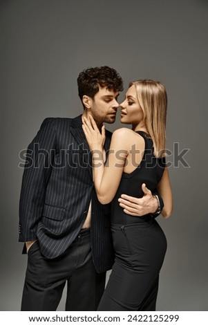 beautiful woman in black attire seducing handsome man in pinstripe blazer on grey backdrop