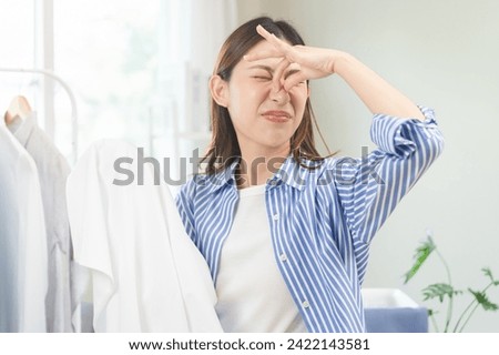 Asian young housewife woman having bad smelling clothes hand holding breath nose with finger, sniff smelly dirty stinky musty, look disgusting from clothes after washed, laundry out of machine at home Royalty-Free Stock Photo #2422143581
