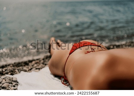 A woman sunbathes on the beach, lying on her stomach in a red swimsuit against the sea backdrop.