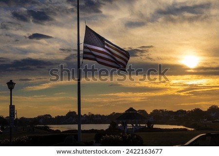 American flag flying half masst with water and sun setting in the background