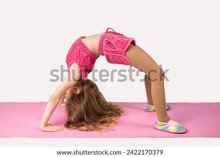 Girl practicing yoga or fitness, standing in Bridge exercise, on a pink yoga mat, working out wearing sportswear, top, shorts, full length picture, white studio background.