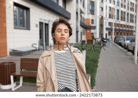 Tired annoyed frustrated offended and resentful female with closed eyes in stylish trench walking down residential area, doing deep breath to avoid feeling of desperation and relieve stress Royalty-Free Stock Photo #2422173873