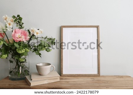 Easter breakfast still life. Blank picture frame mockup. Wooden bench, table composition with cup of coffee, old books. Spring bouquet of pink tulips, white daffodils. Hawthorn. Guelder rose flowers.