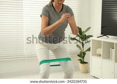 Senior woman doing squats with fitness elastic band at home, closeup