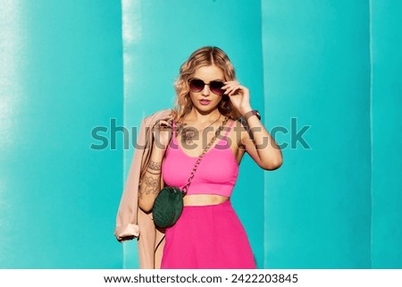 Sunny style fashion portrait of young woman on blue background. Girl wearing cute trendy pink outfit, drinking tasty coffee, enjoy her walk. Fashion style woman doll in pink clothes hold sunglasses.