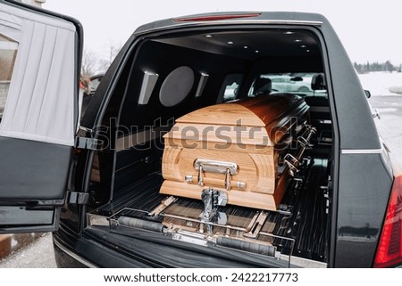 A coffin made of light wood stands in the trunk of a black hearse. Funeral and farewell ceremony. Closeup photo of a funeral casket.