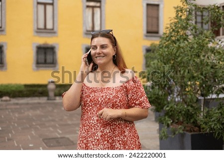 Happy young woman with smartphone calling on city street. Technology, communication and people concept. Positive 30s female speak phone on urban background, old town