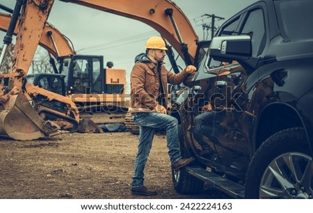 Caucasian Construction Site Supervisor in His 40s Staying Next to His Pickup Truck. Excavators in Background