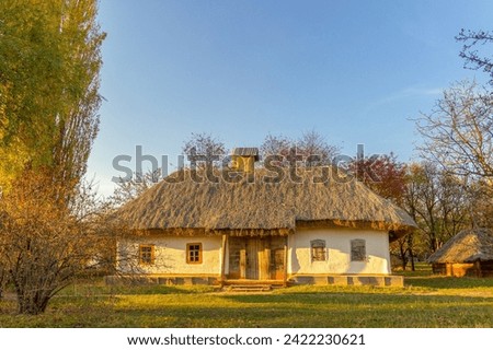 An 18th-century old house with a thatched roof. Autumn landscape, the sun. Historical heritage in the Ukrainian National Open Air Museum Pirogovo. Kiev, Ukraine. Tourism and travel. Royalty-Free Stock Photo #2422230621