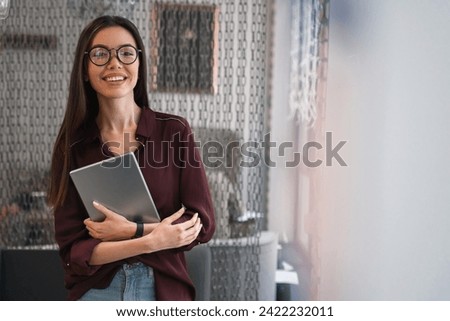 Cheerful woman holding the tablet standing in office. Portrait of happy business woman in casuals in office. HR manager freelancer student teacher working on new project online Royalty-Free Stock Photo #2422232011