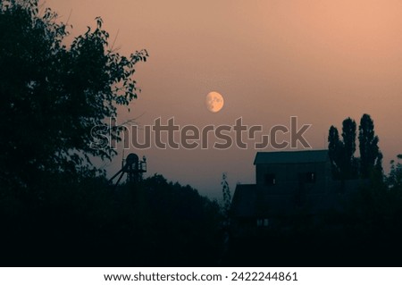Summer rising moon against the backdrop of a weary village