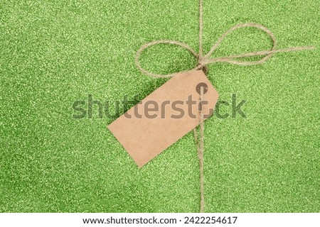 Jute thread with a simple bow and a brown cardboard empty label on green glitter background