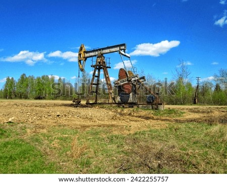  An oil pump jack operates against a clear blue sky in a rural setting
