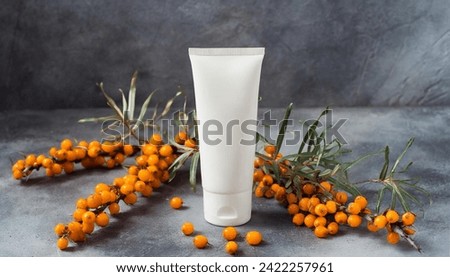 Mockup. White plain tube of cream on a gray background; view from above with an sea buckthorn