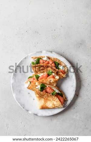Crepes or thin pancakes with smoked salmon, soft cheese and spinach on a plate top view isolated on gray textured background. Pancake day, Maslenitsa. Vertical Royalty-Free Stock Photo #2422265067