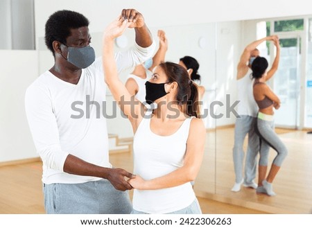 Young adult females and males in masks for disease prevention doing samba partner dance workout during group class in fitness center Royalty-Free Stock Photo #2422306263