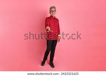 Happy Chinese new year. Asian Chinese energetic senior man wearing red traditional cheongsam qipao or changshan dress with gesture of Greeting,  invitation or welcome isolated on pink background.