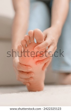 woman having barefoot pain during sitting on couch at home. Foot ache due to Plantar fasciitis and waking longtime. Health and medical concept Royalty-Free Stock Photo #2422325123