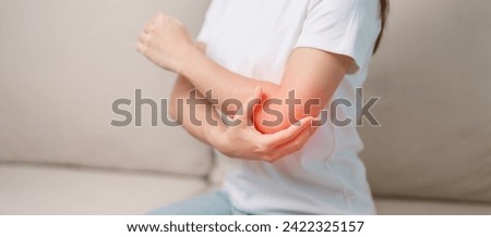Woman having elbow ache during sitting on couch at home, muscle pain due to lateral epicondylitis or tennis elbow. injury, Health and medical concept Royalty-Free Stock Photo #2422325157