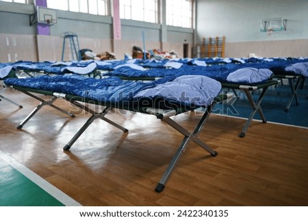 Cots with sleeping bags are placed in the school gym during an emergency Royalty-Free Stock Photo #2422340135