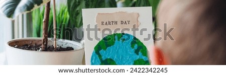 Children's craft for the Earth Day celebration. Little boy holding handmade simple postcard with picture of Planet made of plasticine. Concept of environment education for kids in kindergarten. Banner