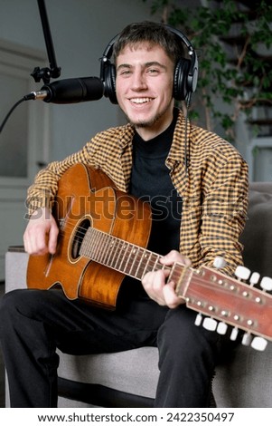 Young man musician singing song playing classical guitar at music studio. Male wearing earphones to sing a song with microphone
