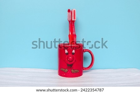 Red toothbrush in red mug cartoon face with copyspace isolated on blue background. Wallpaper red mug and toothbrush on gray table and blue background Royalty-Free Stock Photo #2422354787
