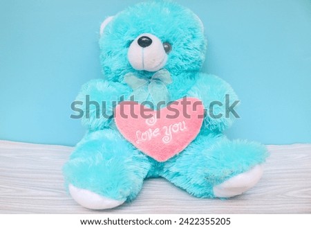 Bright blue bear and pink heart with words I love you on blue background. Bear holding a heart that says I love you