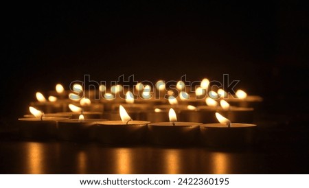 Rows of burning candles. The candles burn against a black backgrounds. The concept of a memorial day. Background for advertising and design projects.