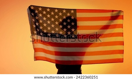 Person silhouette holding big flag against yellow background. Silhouette of man with national flag of usa holding in hands.