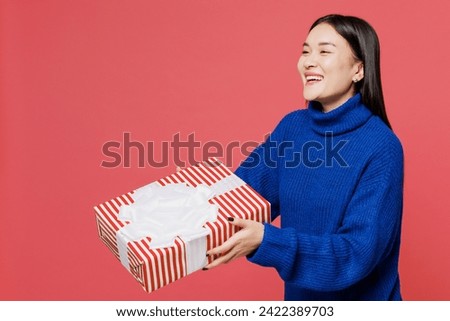 Side view young woman of Asian ethnicity wear blue sweater casual clothes hold give present box with gift ribbon bow isolated on plain pastel light pink background studio portrait. Lifestyle concept