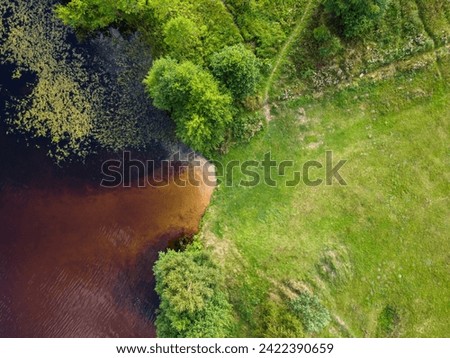 An aerial view captures the gentle confluence of a tawny river with the surrounding verdant landscape, a natural tapestry of earthy hues and vibrant greens. Royalty-Free Stock Photo #2422390659