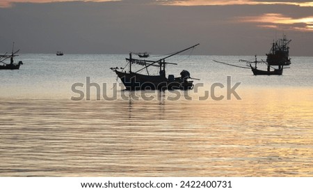 Picture of a fishing boat in the sea Background: The sun is setting in the evening. The sky is orange and gold.
