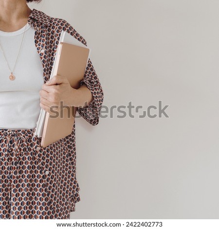 Laptop computer and paper documents in female hand. Young pretty woman in pajamas stays over white wall. Businesswoman, work at home concept Royalty-Free Stock Photo #2422402773