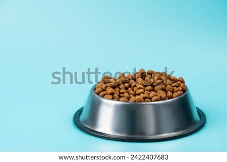 Brown cat or dog kibble in a metal bowl isolated top view close-up. Nutritious healthy diet pet food scattered around, falls and cascades the bowl. Dry cat or dog food spills from a bowl. Royalty-Free Stock Photo #2422407683