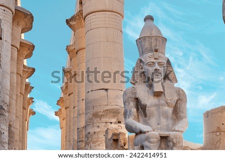 Seated statue of Ramesses II by the First pylon of the Luxor Temple, Egypt. Columns and statues of the Luxor temple main entrance, first pylon, Egypt Royalty-Free Stock Photo #2422414951