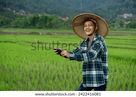 Asian male agricultural researcher is taking photo rice plants to inspect and do research about growth, diseases, insects at paddy field. concept : Smart farmer. Use technology device in agriculture.