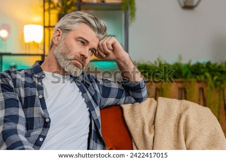 Disappointed man sits at home reflecting on moral distress after quarrel break-up or divorce problem feeling bad annoyed ill sick. Sad middle-aged guy in room contemplates the emotional aftermath Royalty-Free Stock Photo #2422417015