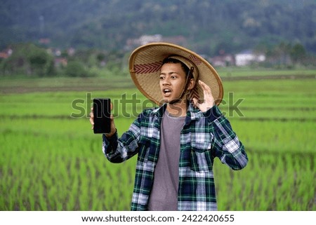 Young Indonesian farmer Showing a mobile screen at green agriculture field. agriculture technologi concept