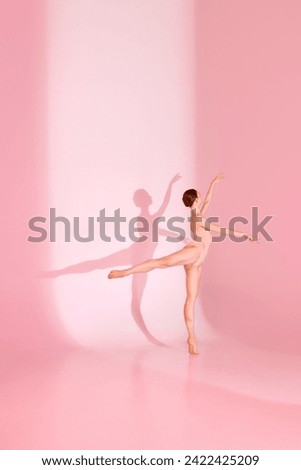 Ballet in Blush. Graceful dancer, dressed in pink swimsuit, poses barefoot against pastel pink background. Her shadow mirrors her elegance. Concept of poise, beauty, ballet, gracefulness.
