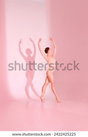 Pastel Ballet. Woman gracefully poses in pink swimsuit against soft pink backdrop. Her barefoot silhouette casts shadow, echoing her elegant movements. Concept of ballet, grace, beauty.