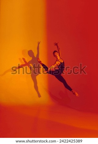 Elegant Motion in Neon. Graceful dancer poses in black sports overalls, barefoot against gradient red-orange backdrop, her shadow adding depth to her movements. Concept of grace, athleticism, motion.