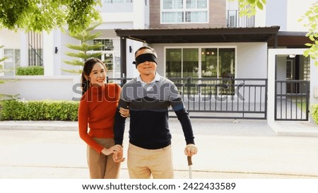Beautiful eldest daughter covered her eyes with black cloth surprise retired old man standing together in front house buying new house present give happiness with new luxurious and expensive house.