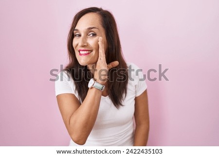 Middle age brunette woman standing over pink background hand on mouth telling secret rumor, whispering malicious talk conversation  Royalty-Free Stock Photo #2422435103