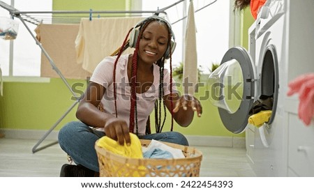 Joyous african american woman listening to soulful music, washing clothes with a gleaming smile in a cozy laundry room