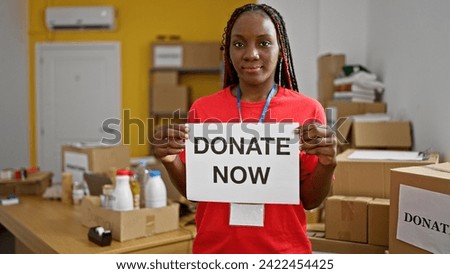 Serious-faced african american woman volunteer holding 'donate now' sign at charity center, encouraging community donation